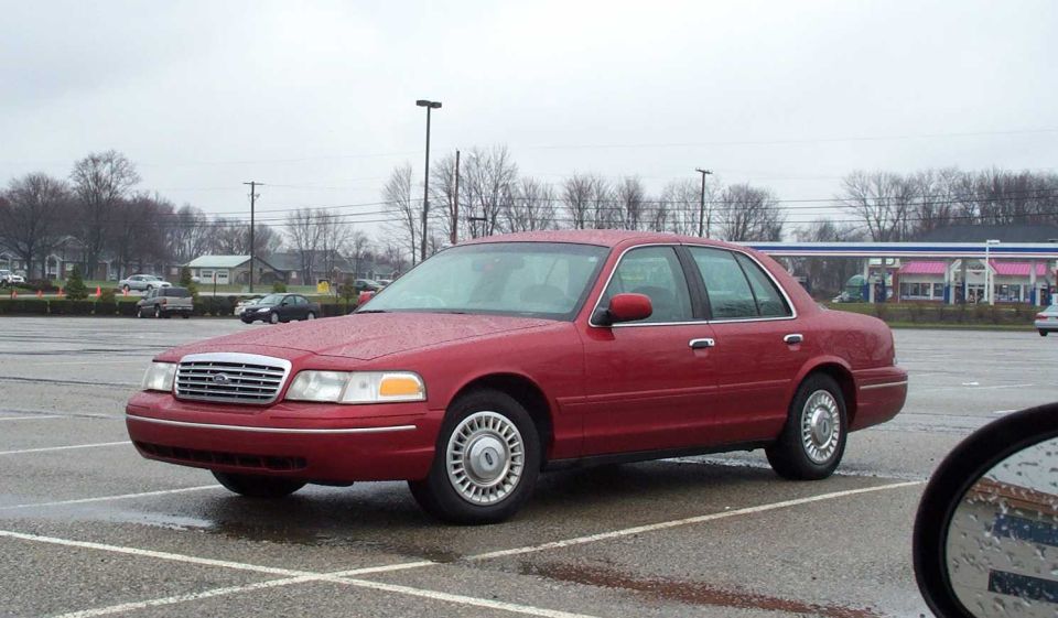 Dark red Ford Crown Victoria sedan, front three-quarter view in a wet parking lot