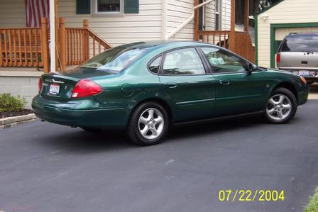 2000 Ford Taurus - A green 2000 Ford Taurus sedan is parked in a driveway next to a house and garage.