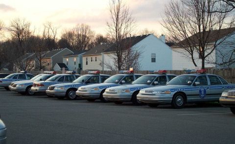 1998 Ford Crown Victoria - A row of silver Ford Crown Victoria police cruisers are parked in a lot, with emergency lights visible on their roofs.