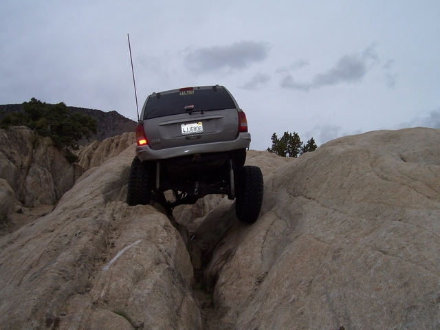 Gray Jeep Grand Cherokee with lifted suspension and off-road tires navigating a rocky trail from the rear