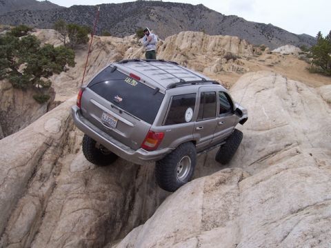 1989 Ford Bronco - A modified Jeep Grand Cherokee navigates a rocky trail with a person standing on its roof.