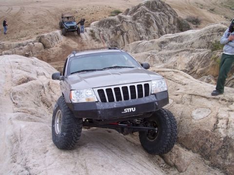 1989 Ford Bronco - A Jeep Grand Cherokee tackles a challenging off-road course with other vehicles in the background.