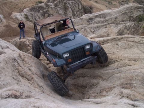 1989 Ford Bronco - A green Jeep Wrangler tackles a challenging rocky off-road course.