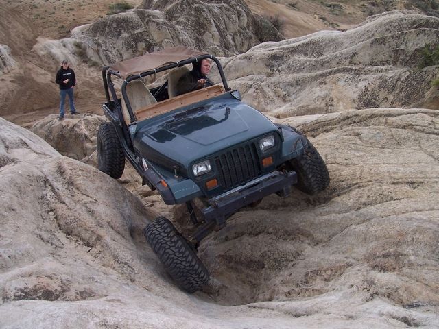 Green Jeep Wrangler navigating rocky terrain, front view