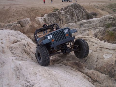 1989 Ford Bronco - Jeep Wrangler tackling a rocky trail, with other people and vehicles in the distance.