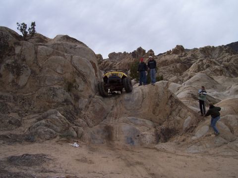 1989 Ford Bronco - People watch an off-road vehicle navigate a rocky landscape under an overcast sky.