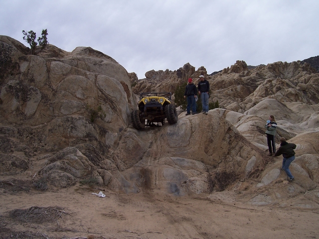 Yellow off-road vehicle climbing rocks with people watching