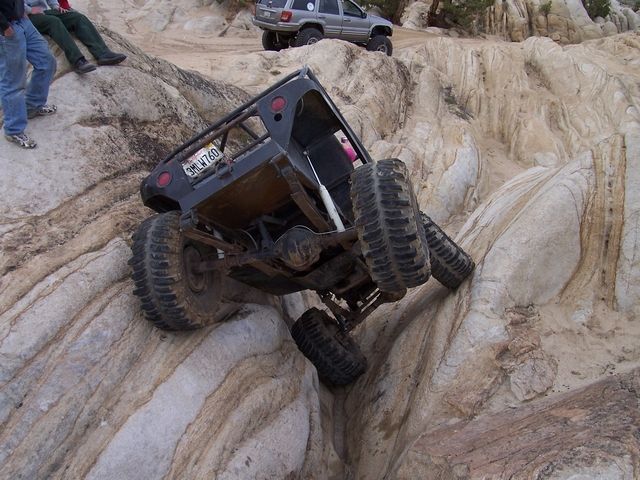 Black off-road vehicle with roll cage tilted on a rock face, license plate 3HLW760 visible
