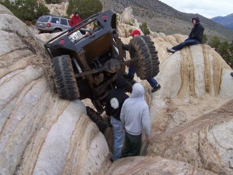 1989 Ford Bronco - An off-road vehicle is stuck on rocks with several people observing the situation.