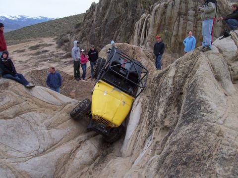 1989 Ford Bronco - A yellow off-road vehicle is stuck on its side in a rocky area, with spectators observing the scene.
