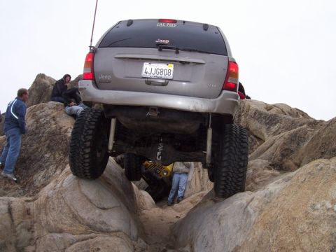 1989 Ford Bronco - A lifted Jeep Grand Cherokee tackles a challenging rocky trail, with another vehicle visible behind it.