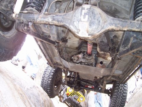1989 Ford Bronco - The underside of a heavily modified off-road vehicle is shown, with another vehicle partially visible beneath it.