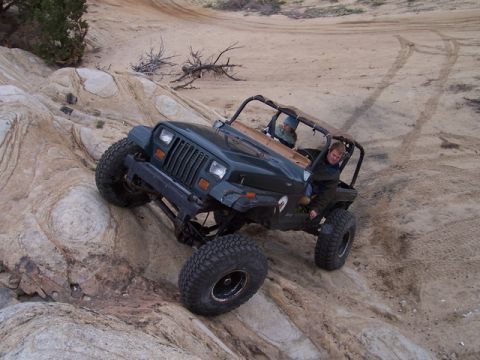 1989 Ford Bronco - A dark green Jeep Wrangler navigates a challenging rocky terrain during an off-road excursion.