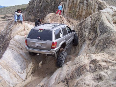 1989 Ford Bronco - A Jeep Grand Cherokee navigates a rocky trail with onlookers observing the challenging off-road maneuver.
