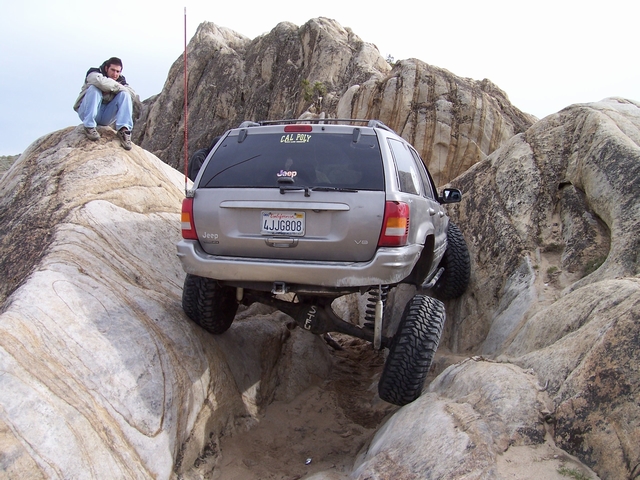 Silver Jeep Grand Cherokee climbing a granite rock notch, rear view with lifted suspension