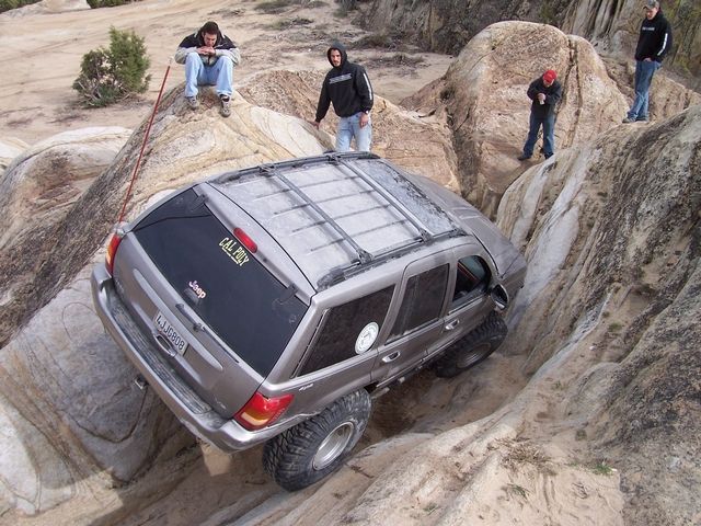 Jeep Grand Cherokee with large tires navigating a rocky off-road trail, people watching from above