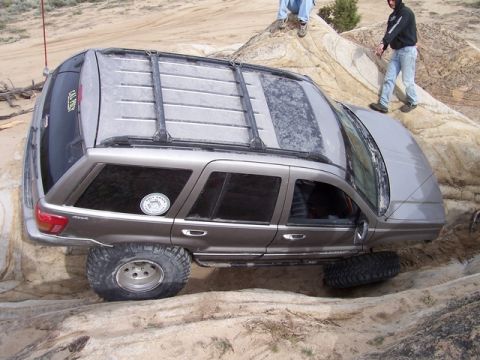 1989 Ford Bronco - This Jeep Grand Cherokee is navigating a rocky off-road trail, with two people observing its progress.