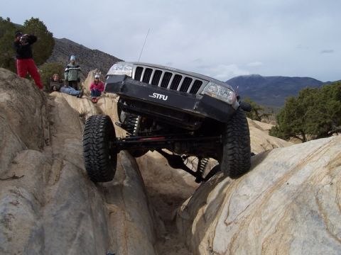 1989 Ford Bronco - Modified Jeep Grand Cherokee navigating a rocky trail with spectators observing.