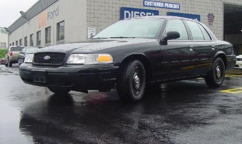2003 Ford Crown Victoria - A black 2003 Ford Crown Victoria is parked outside a building with 'Ford' signage.