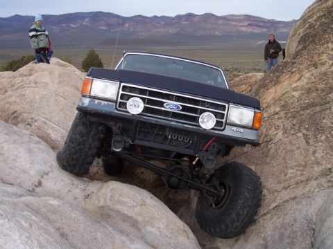 1989 Ford Bronco - A Ford Bronco navigates a rocky trail with two people watching in the background.