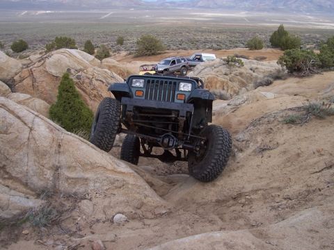 1989 Ford Bronco - A dark green Jeep Wrangler navigates a rocky trail with other vehicles in the background.