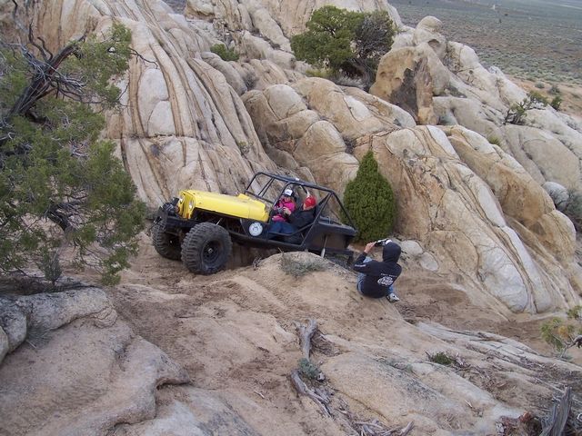 Yellow buggy with roll cage climbing rocky terrain. Person filming from below