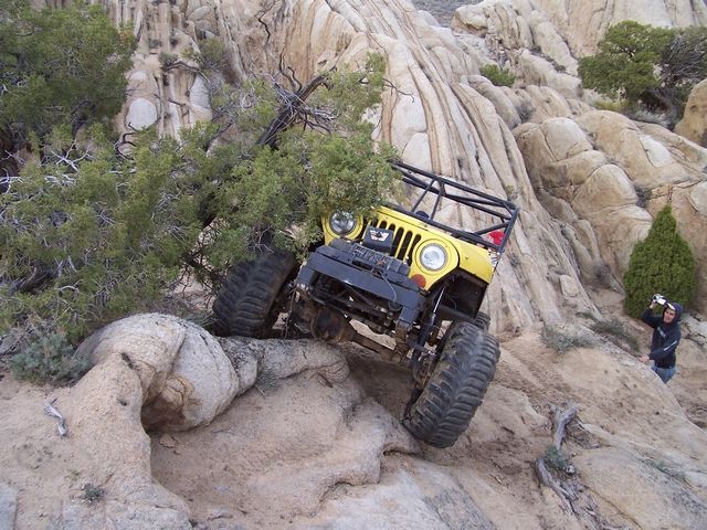 Yellow off-road vehicle with a roll cage climbing over rocks and brush