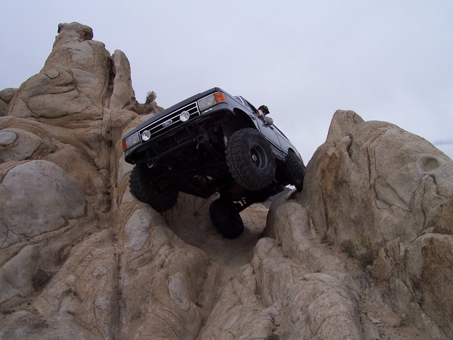 Lifted dark blue Ford Bronco climbing a steep sandstone rock ledge