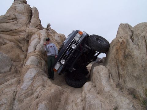 1989 Ford Bronco - A person stands next to a Ford Bronco that is precariously balanced on rocks, appearing stuck.