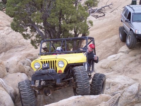 1989 Ford Bronco - A yellow off-road jeep tackles a challenging rocky trail, with another SUV visible in the background.
