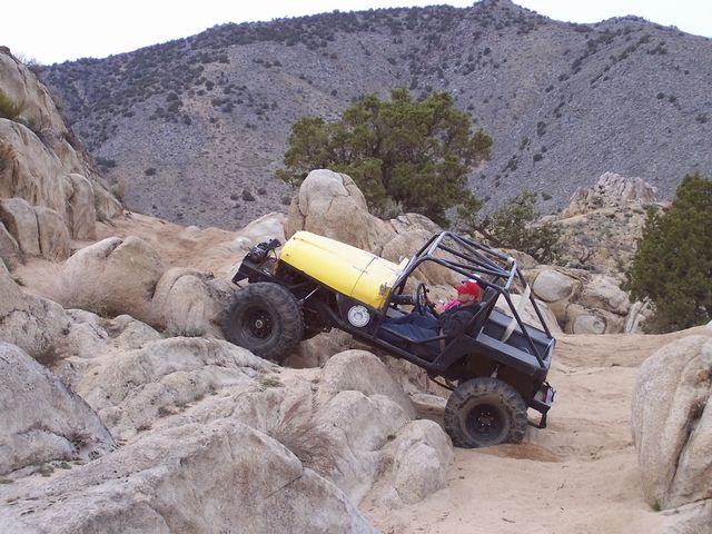 Yellow-hooded caged Jeep rock buggy tipping off a boulder on a desert granite trail