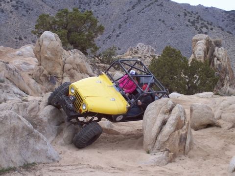 1989 Ford Bronco - Off-road vehicle with roll cage traversing a rocky desert landscape.