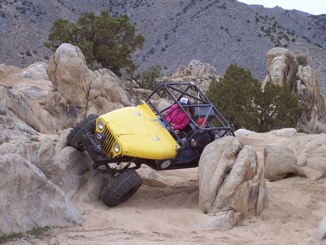 Yellow tube-frame rock buggy flexing over a granite ledge in a desert canyon