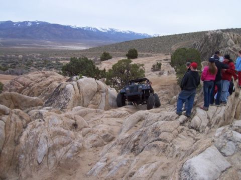 1989 Ford Bronco - Off-road enthusiasts watch a Jeep Wrangler tackle a challenging rocky course in a desert landscape.