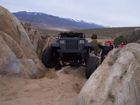 1989 Ford Bronco - A Jeep Wrangler tackles a challenging off-road course with spectators watching in the background.