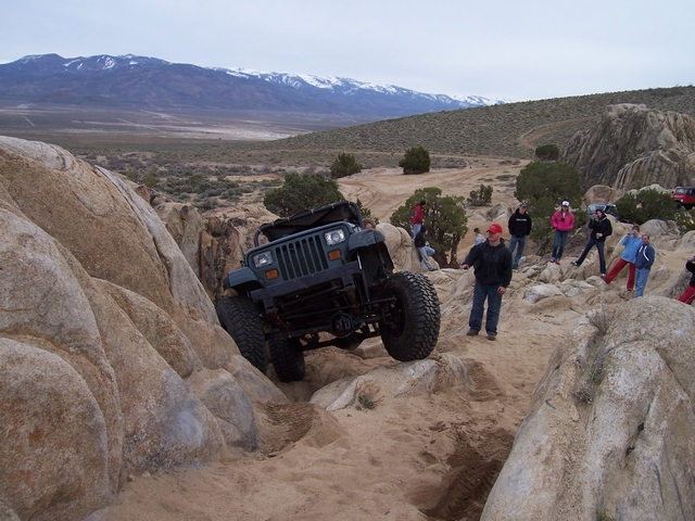 Jeep Wrangler climbing over rocks with people watching in the background