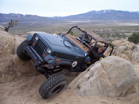 1989 Ford Bronco - A Jeep Wrangler navigates a rocky desert terrain, with two occupants inside the vehicle.
