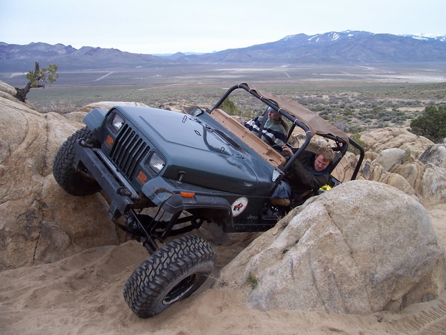 Jeep Wrangler climbing over rocks in a desert landscape with two people inside