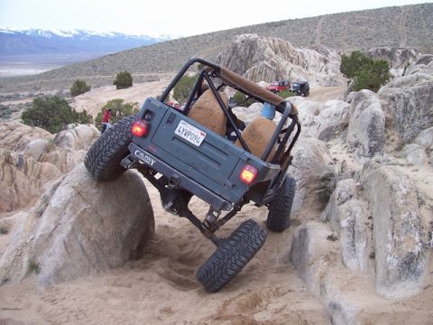 1989 Ford Bronco - A Jeep Wrangler TJ navigates a rocky trail, demonstrating its off-road capabilities. Another vehicle is visible in the background.