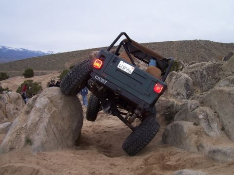 1989 Ford Bronco - Off-road Jeep Wrangler climbing over large rocks in a desert landscape.