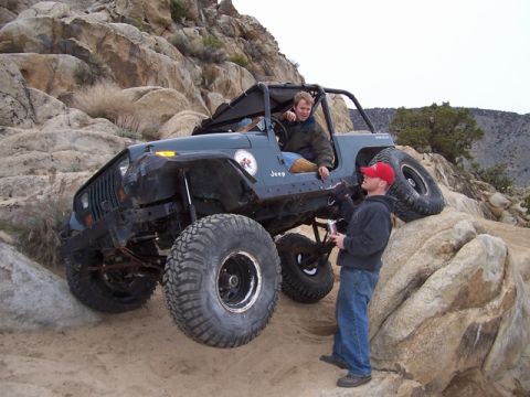 1989 Ford Bronco - A modified Jeep navigates a challenging rocky trail, with two individuals observing its progress.