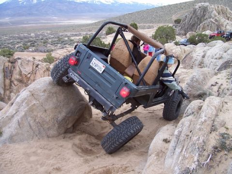 1989 Ford Bronco - A green Jeep Wrangler navigates a rocky off-road course with mountains in the background.