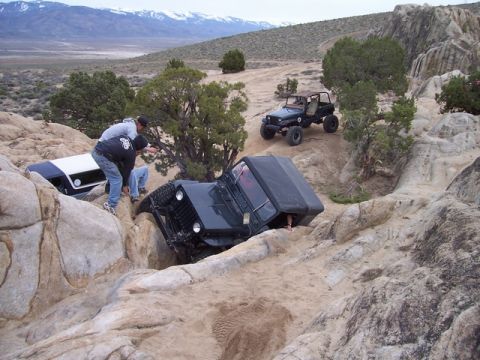1989 Ford Bronco - Two Jeeps navigate a challenging rocky terrain, with one vehicle stuck in a deep crevice.