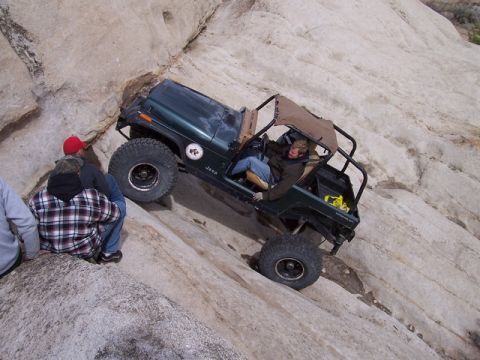 1989 Ford Bronco - A green Jeep Wrangler navigates a steep, rocky terrain with onlookers observing the off-road challenge.