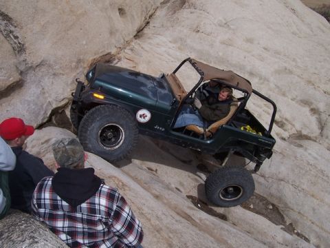 1989 Ford Bronco - Jeep Wrangler tackling a challenging rocky trail with spectators observing the off-road action.