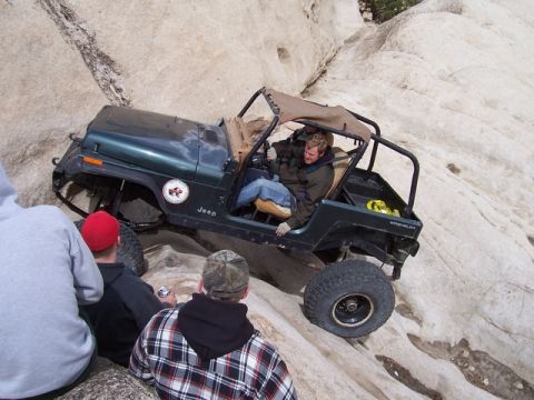 1989 Ford Bronco - A Jeep Wrangler navigates a rocky incline, with several onlookers observing the off-road maneuver.
