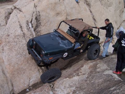 1989 Ford Bronco - A Jeep Wrangler navigates a rocky incline with onlookers present.