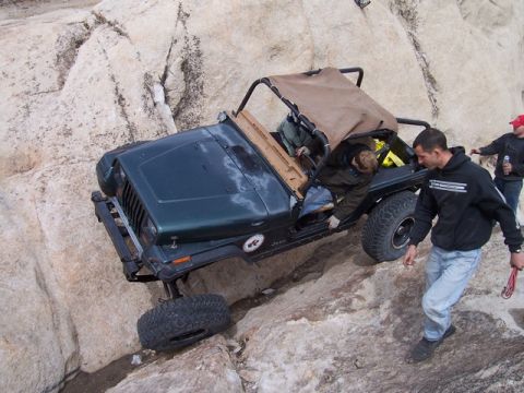 1989 Ford Bronco - A dark green Jeep Wrangler navigates a rocky incline with assistance from onlookers.