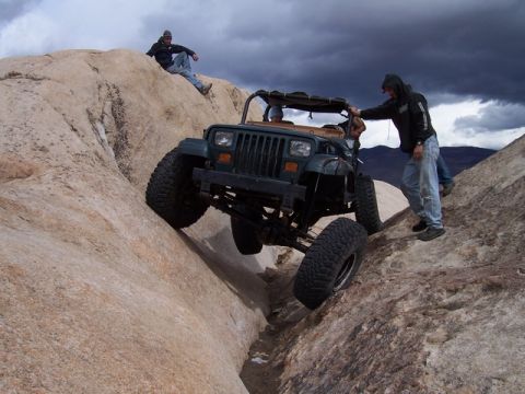 1989 Ford Bronco - A Jeep Wrangler navigates a challenging rocky terrain, with onlookers observing the off-road adventure.