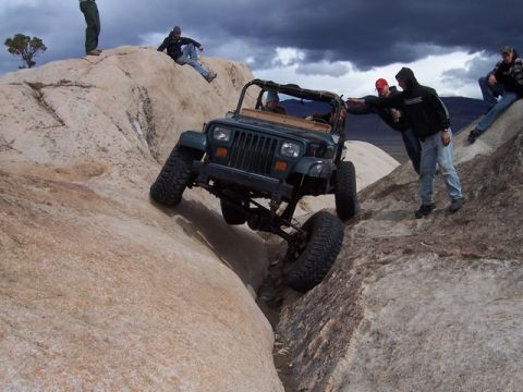 1989 Ford Bronco - A Jeep Wrangler navigates a challenging rocky terrain with onlookers observing the off-road adventure.